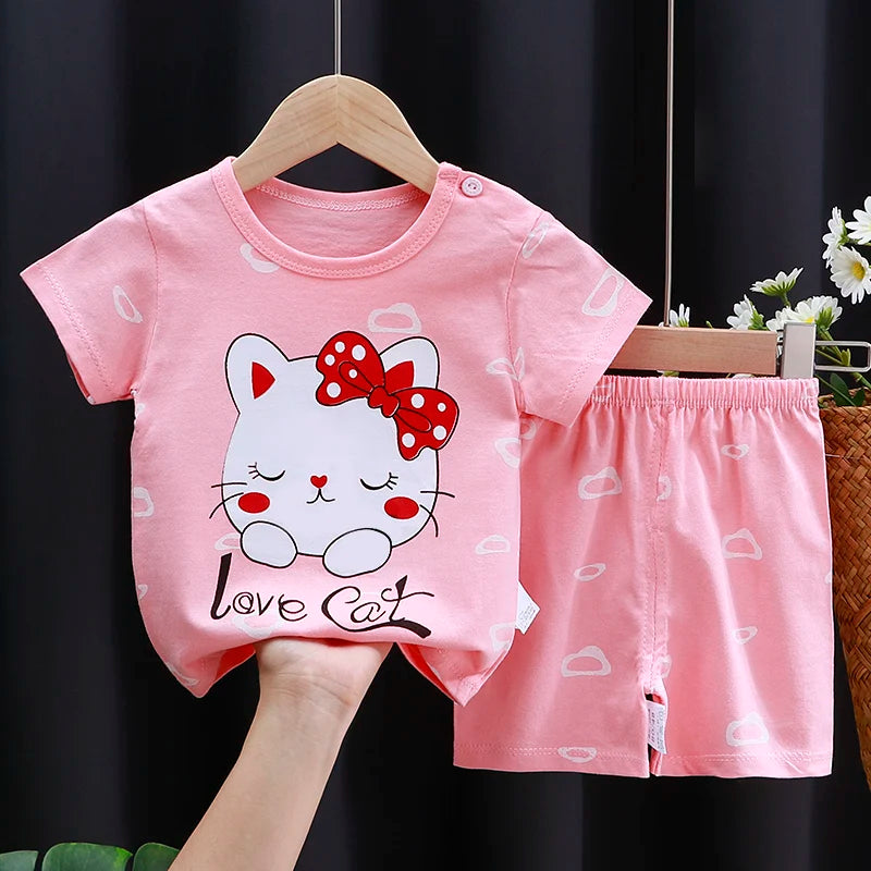 Pink children's outfit with a cartoon cat design on a hanger against a dark background.