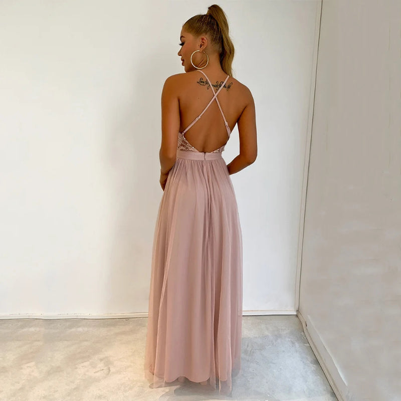 Woman wearing a long, light pink dress with thin straps against a white wall.