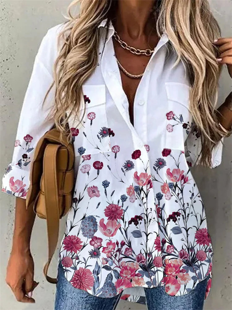 Woman wearing a white blouse with floral patterns, holding a brown bag against a neutral background.