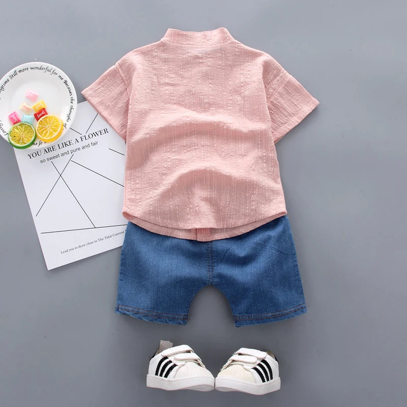 Children's outfit with pink shirt, blue shorts, and white sneakers on a gray background