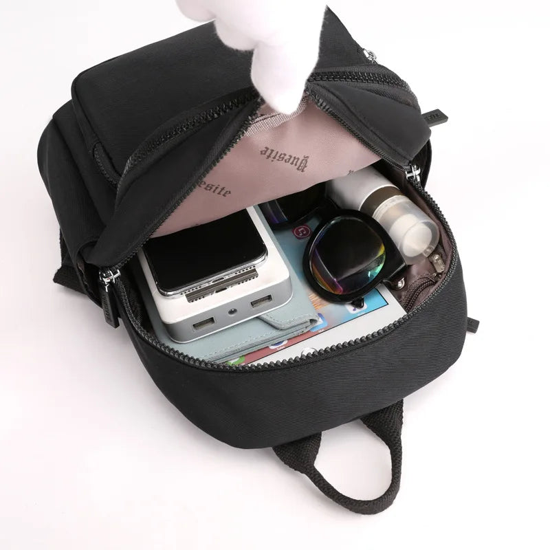 Black backpack with items like a phone, wallet, and sunglasses inside on a white background