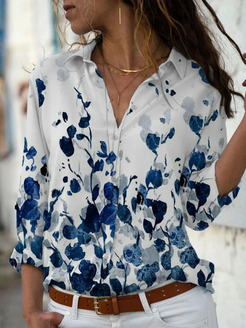 Woman wearing a white shirt with blue floral pattern, white pants, and brown belt.