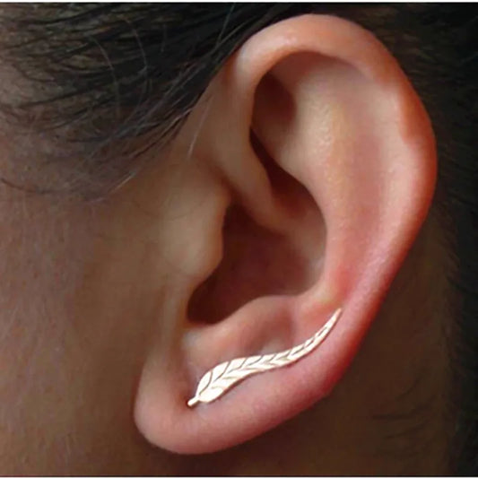 Gold leaf-shaped earring worn on an ear with a dark background