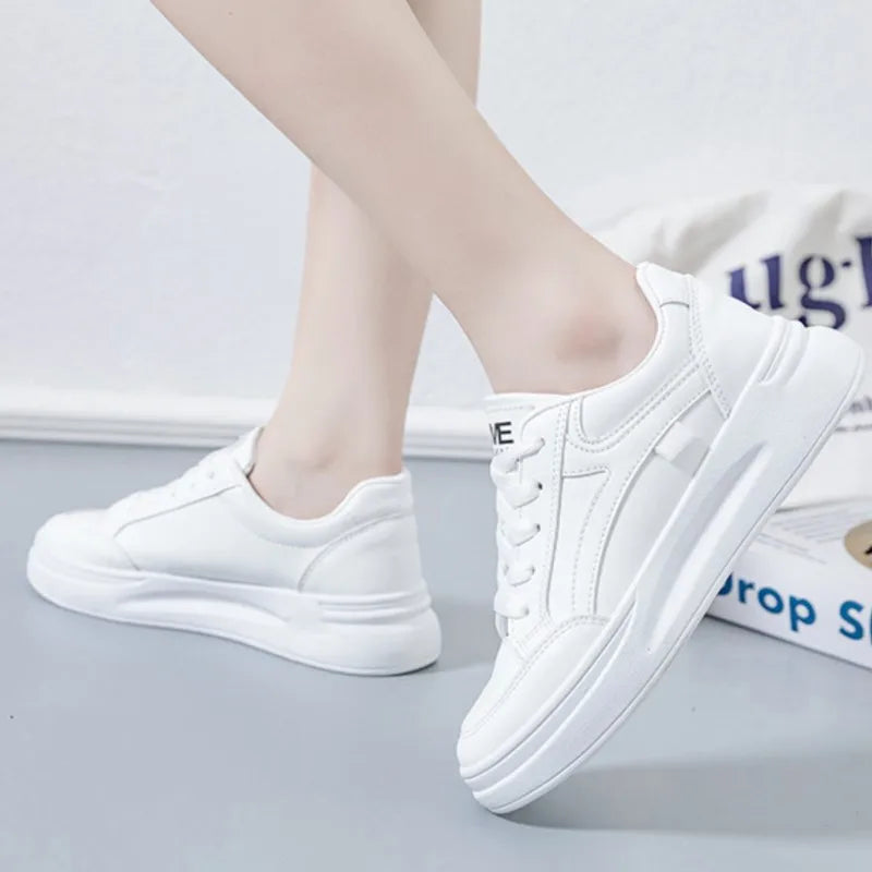 White sneakers worn by a person on a light gray surface with a white background