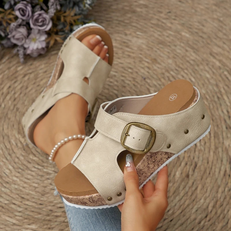 Beige sandal with a brown sole worn by a person on a textured surface