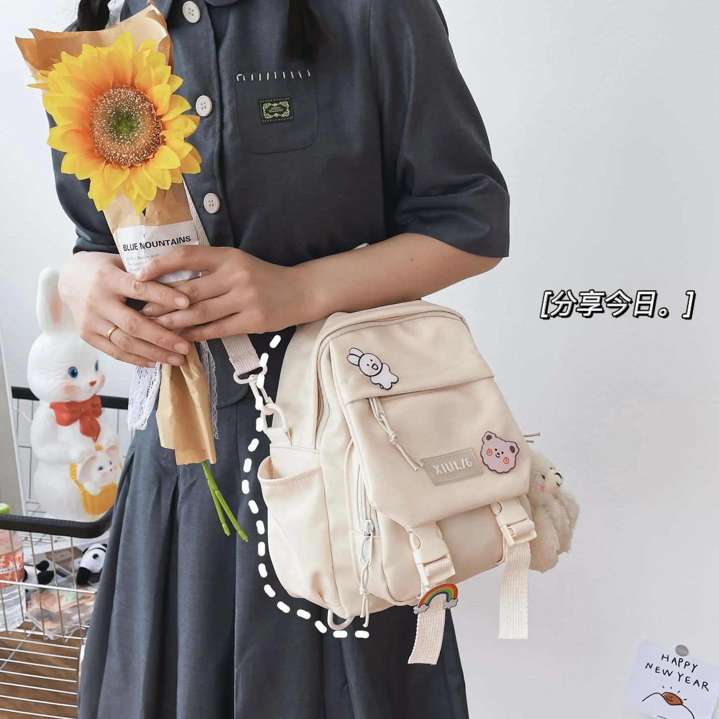Person holding a sunflower and a beige backpack with cartoon character designs on a white background.