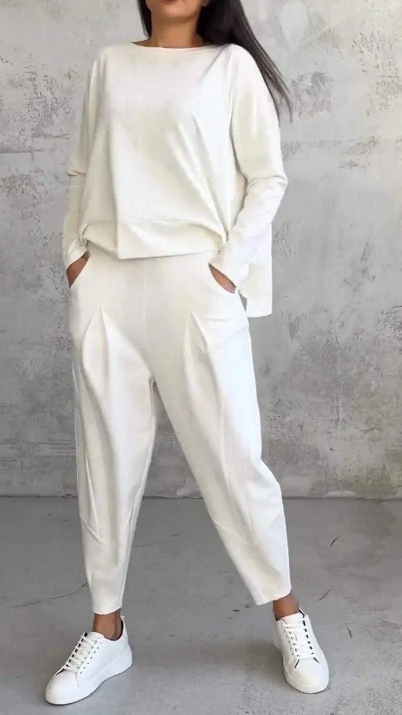 Person wearing a white outfit with high-waisted pants against a gray concrete wall.
