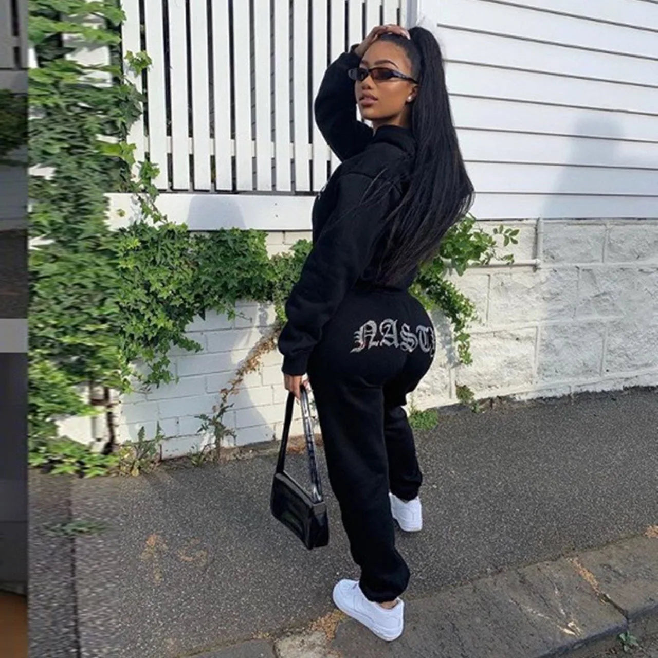 Person wearing a black outfit with 'NASTY' text, standing outdoors.