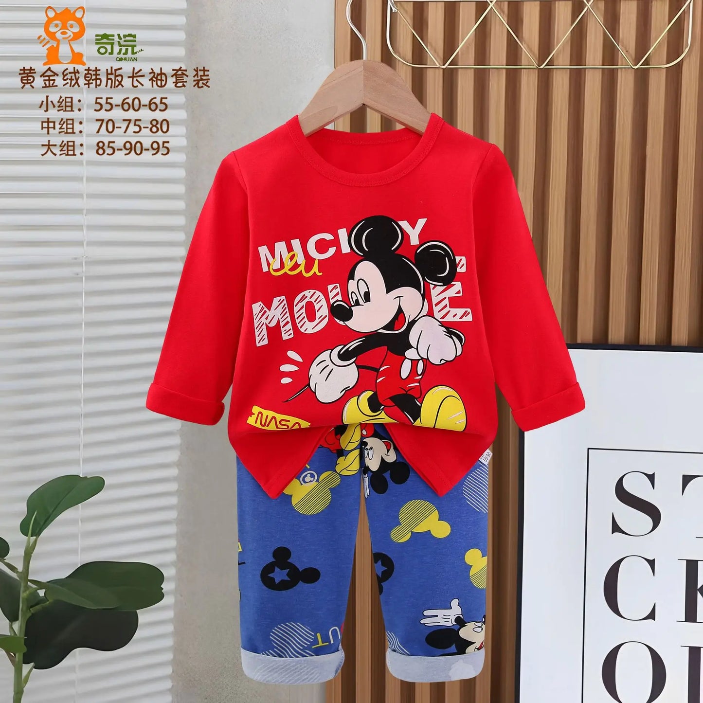 Red long-sleeve shirt with Mickey Mouse design and blue pants on a hanger against a white wall.
