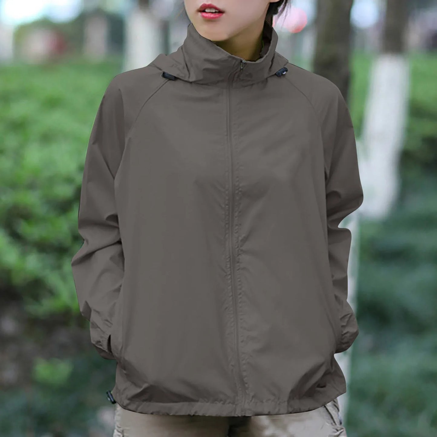Person wearing a brown jacket in an outdoor setting with blurred greenery