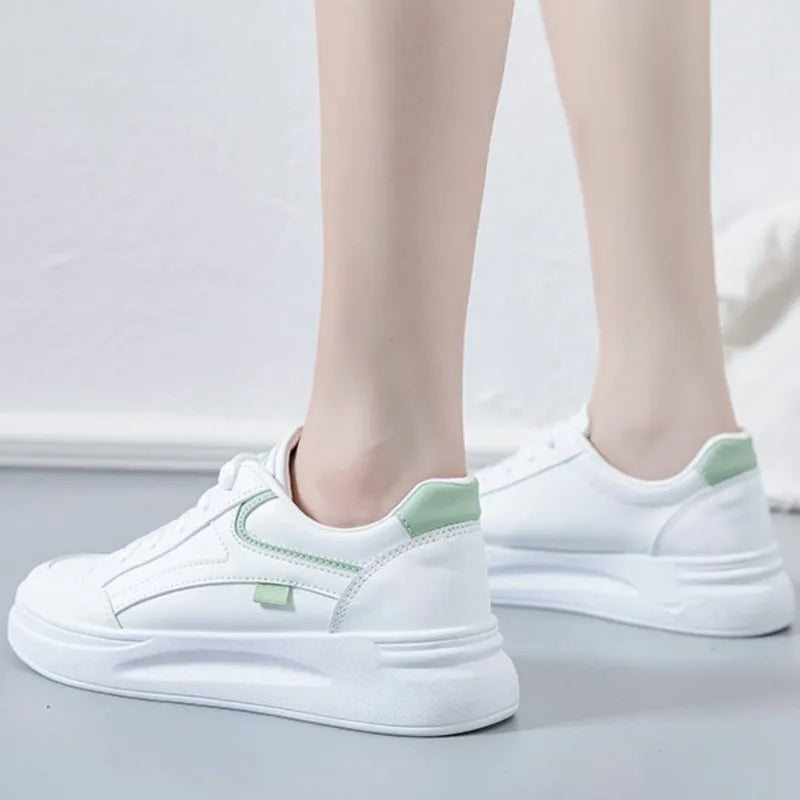 White sneakers with green accents worn by a person on a light gray background
