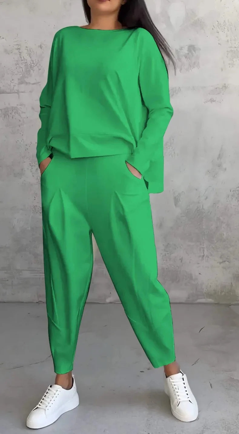 Person wearing a green outfit with white sneakers against a gray concrete wall.