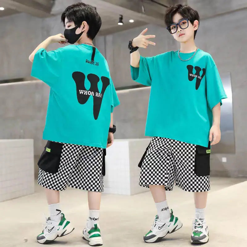 Two children wearing matching teal shirts with black graphics and checkered shorts in an indoor setting.