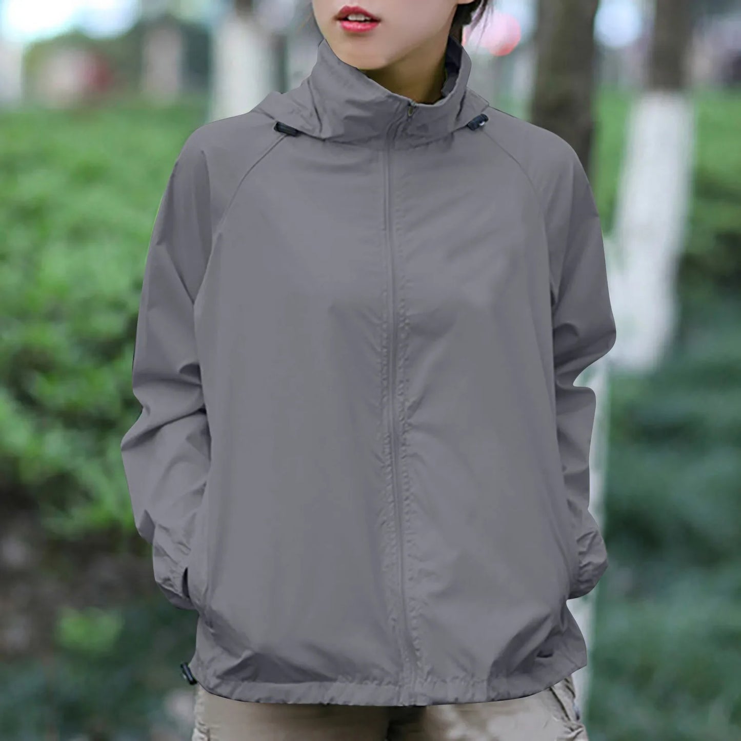 Person wearing a gray jacket in an outdoor setting with greenery.