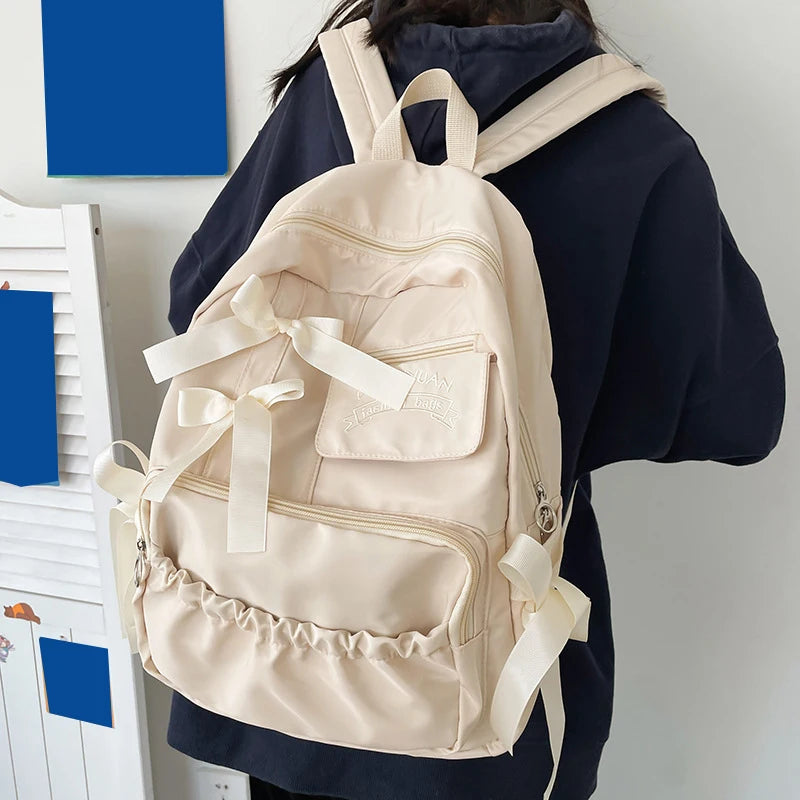 Beige backpack with ribbons worn by a person against a white background
