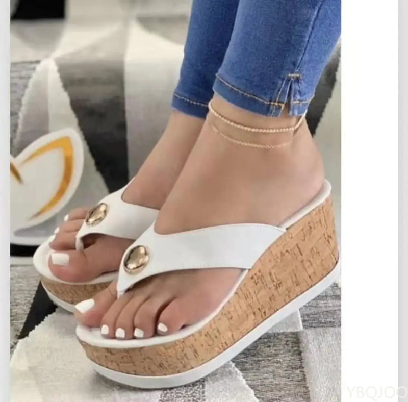 White wedge sandals with cork sole worn by a person, on a neutral background