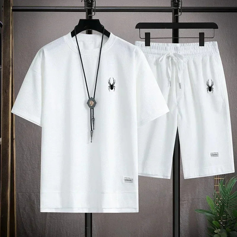 White t-shirt and shorts set with spider logo on hangers against a gray background