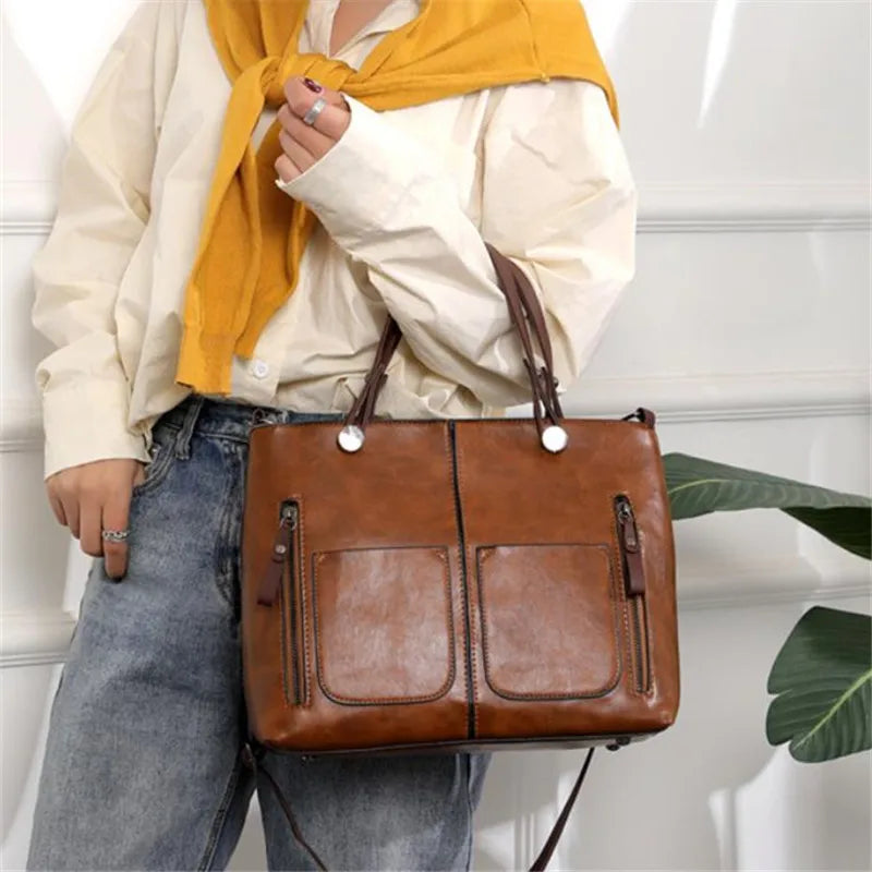 Person holding a brown leather handbag with a neutral background