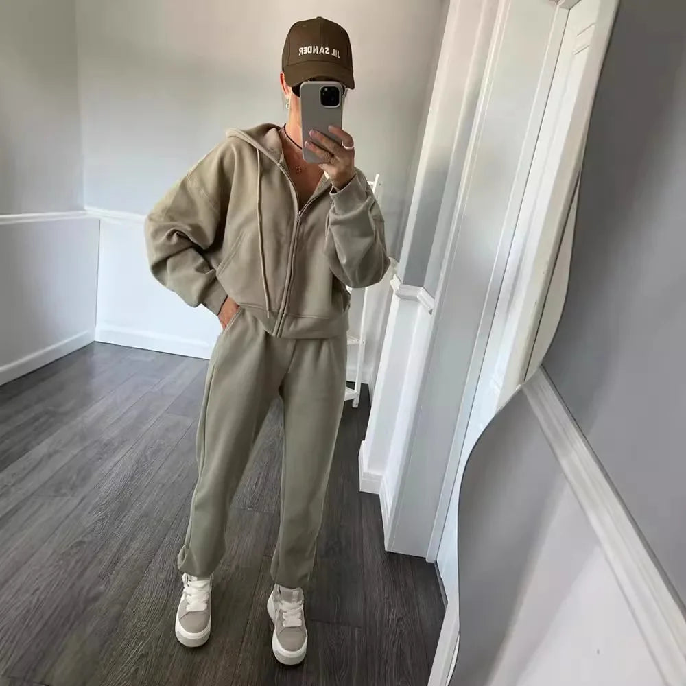 Person wearing a gray tracksuit and cap in a room with gray walls and wooden floor.
