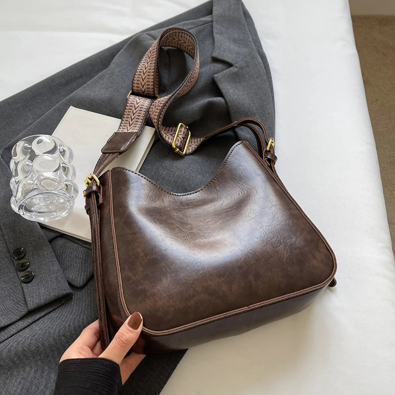 Brown leather handbag held by a hand with a gray coat and glass mug in the background