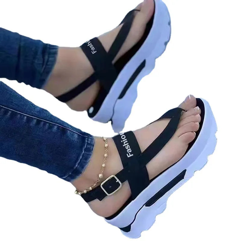 Black sandals with white soles worn by a person in jeans on a white background