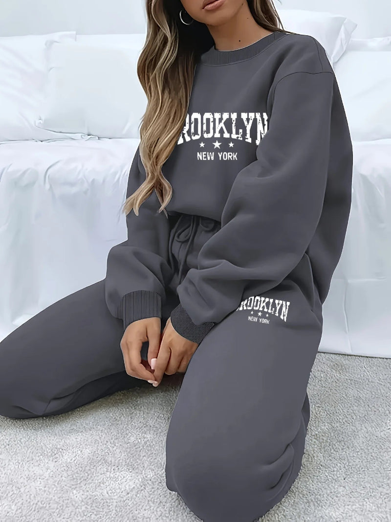 Person wearing a gray 'Brooklyn New York' sweatshirt and pants sitting on a white couch.