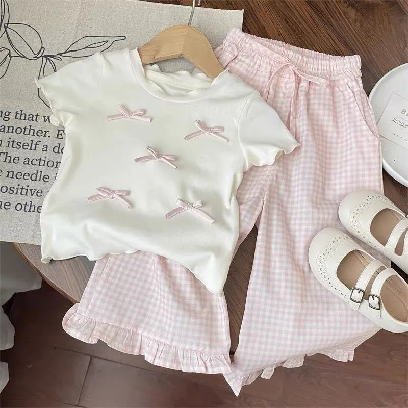 Children's outfit with white top and pink checkered shorts on a wooden surface.