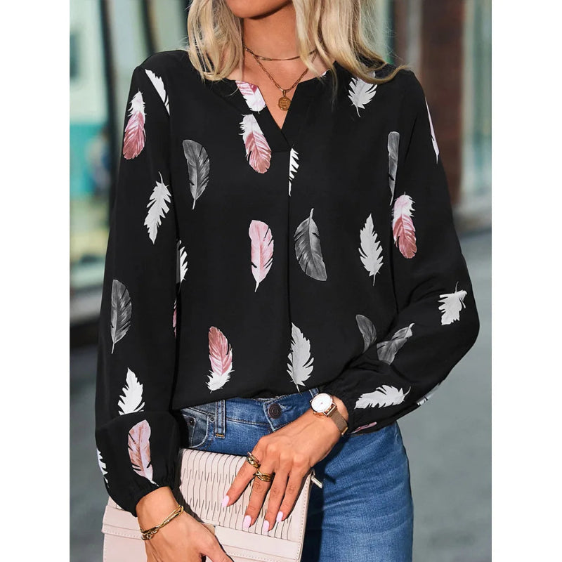 Woman wearing a black blouse with feather pattern, blue jeans, and holding a clutch.