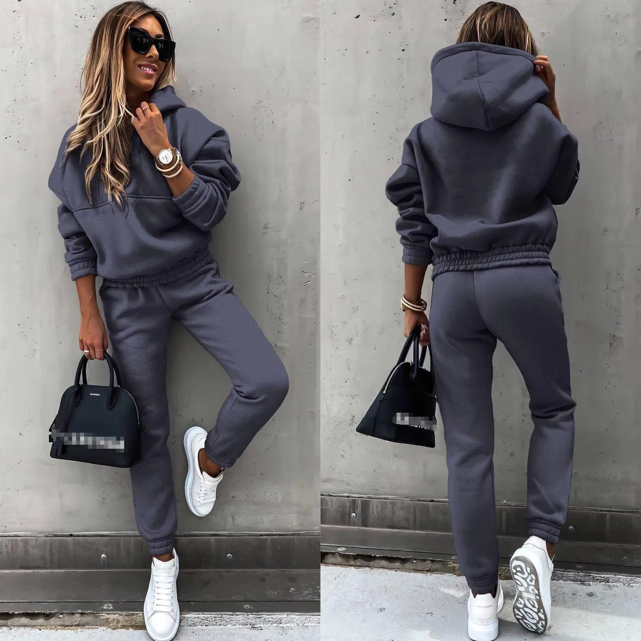 Woman wearing a gray tracksuit with sunglasses and a black handbag against a concrete wall.