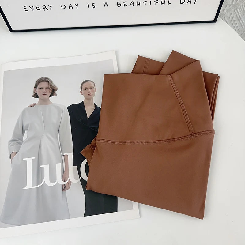 Brown leather jacket on a white surface with a magazine featuring two models and the brand 'Lululemon' in the background.