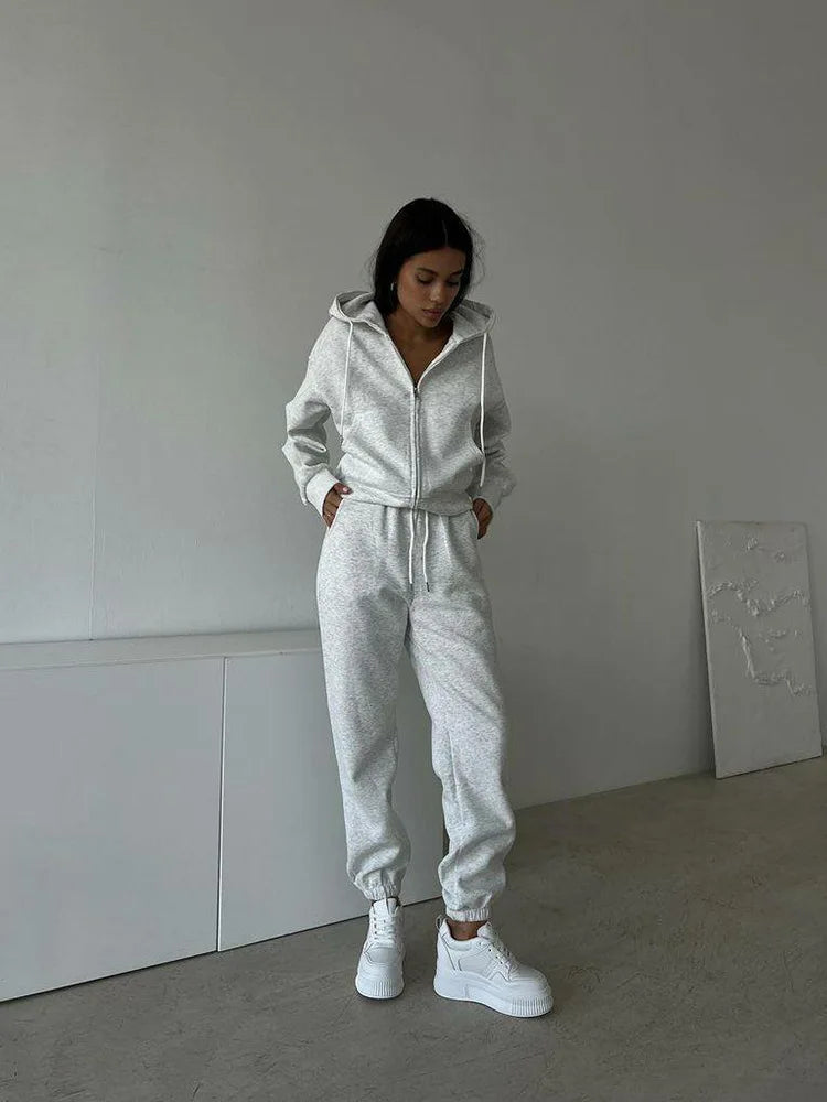 Person wearing a gray tracksuit with white sneakers in a minimalistic room.