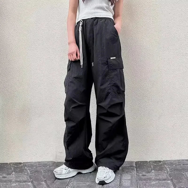 Person wearing black cargo pants with zippers against a light gray wall.