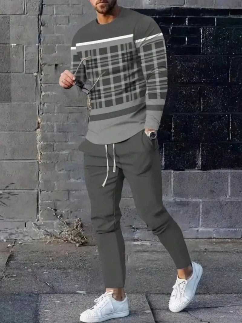 Person wearing a plaid sweater and green pants against a brick wall.