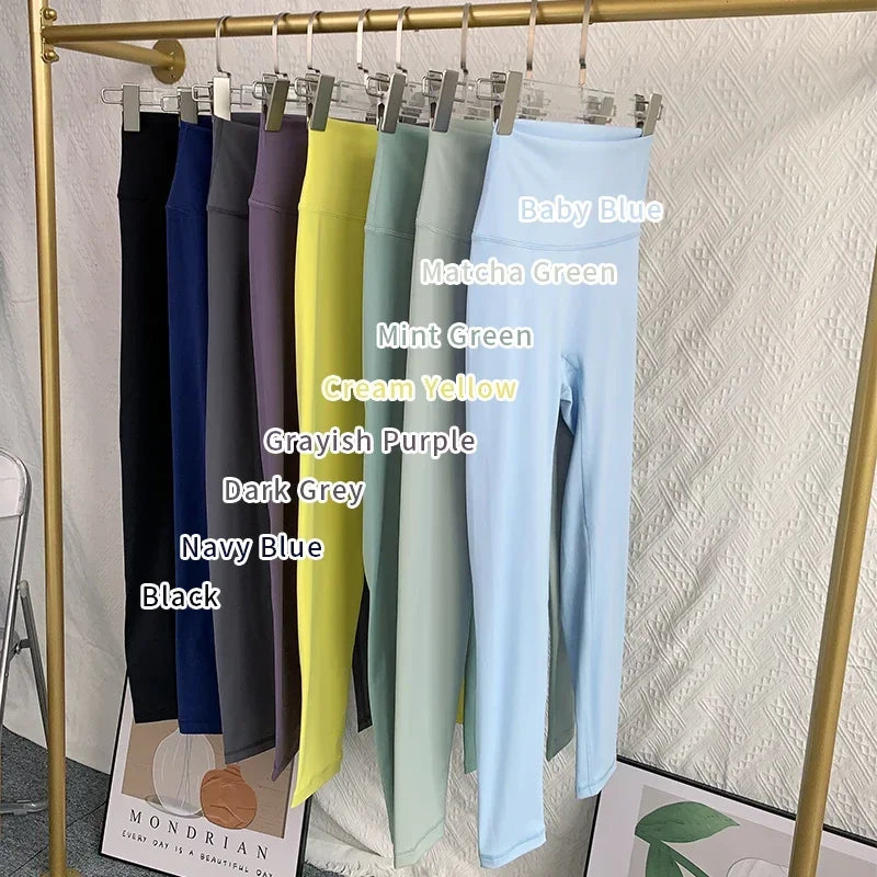 Hanging pants in various colors with labels on a gold rack against a textured white wall.