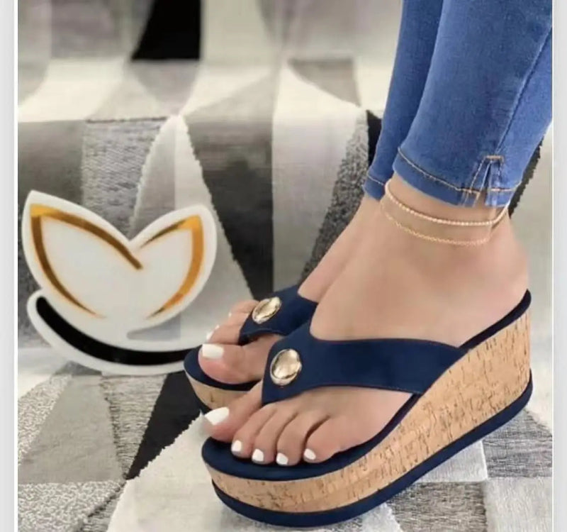 Navy blue wedge sandals with gold buttons worn by a person on a gray surface.