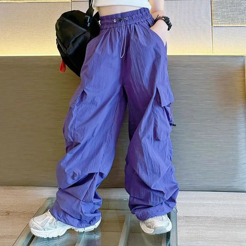 Person wearing purple cargo pants and white sneakers on a wooden floor.