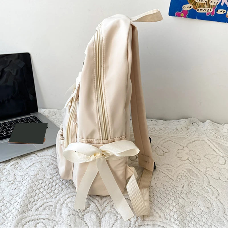 Beige backpack with ribbons on a white surface next to a laptop