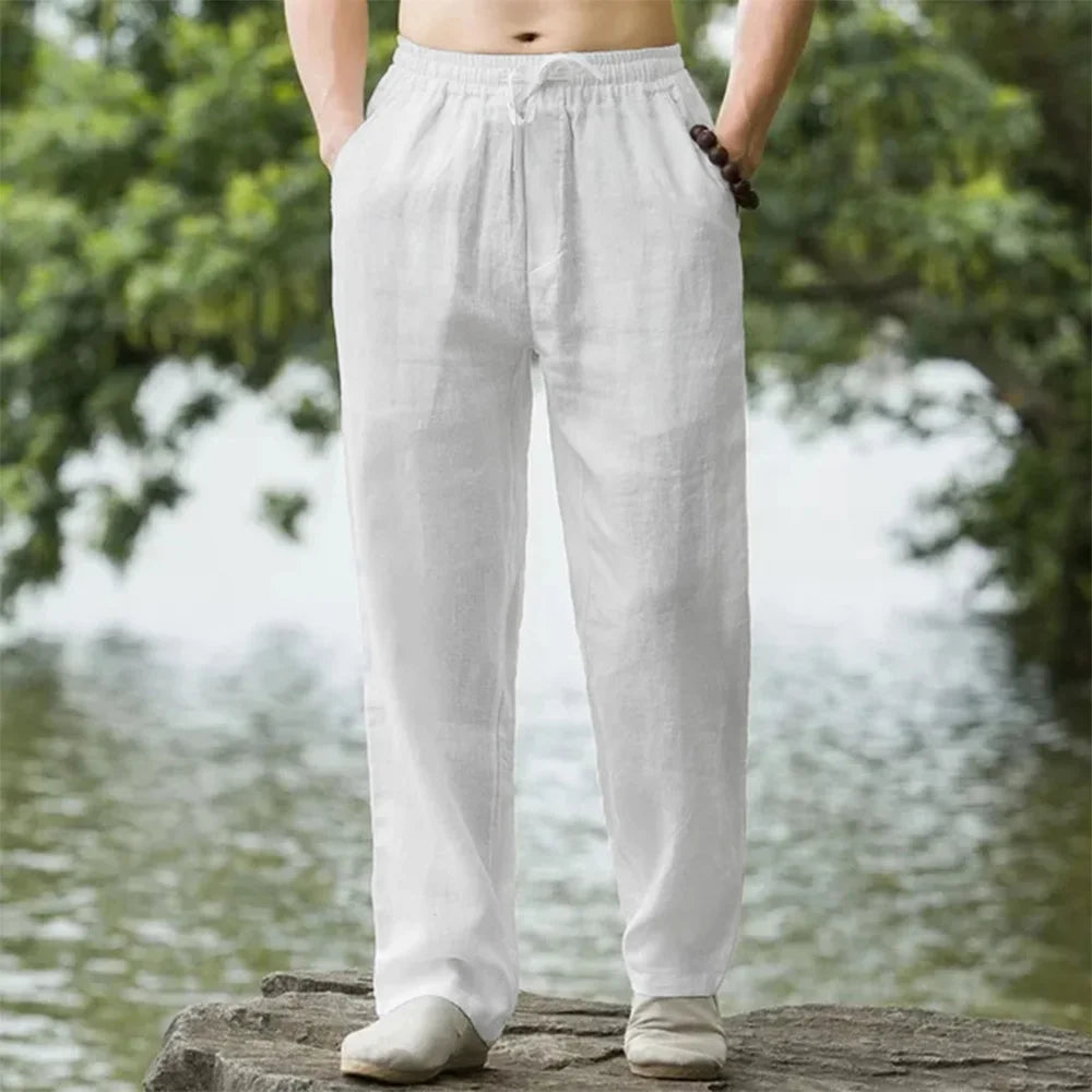 Person wearing light gray pants standing by a body of water with greenery.
