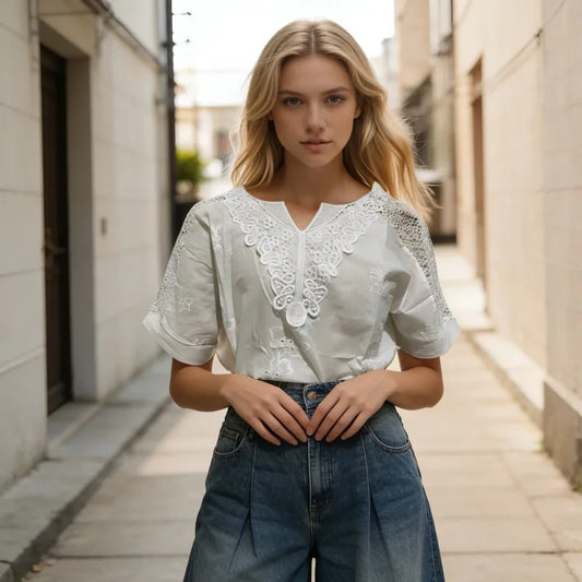Woman wearing a white lace top and blue jeans standing in an urban alleyway.