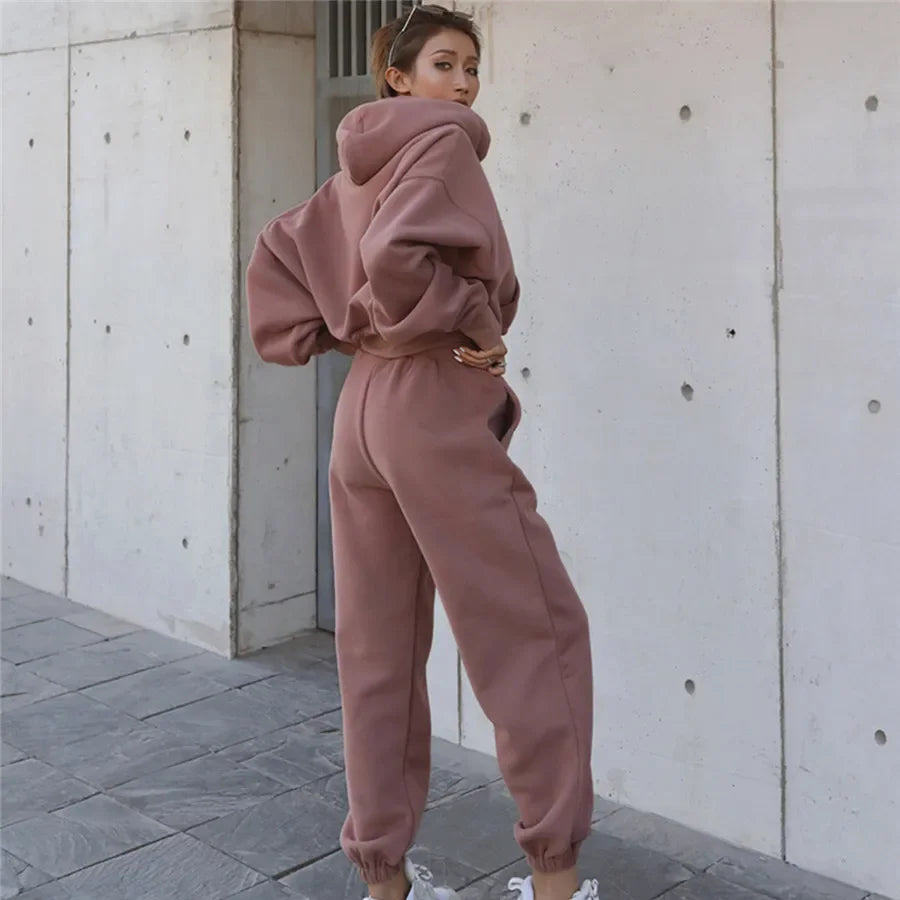 Person wearing a pink tracksuit standing against a concrete wall.