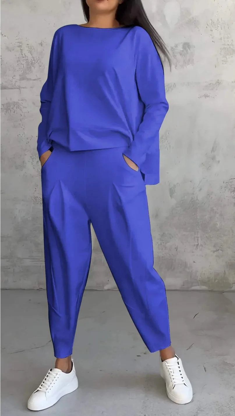 Person wearing a blue outfit with white sneakers against a gray concrete wall.