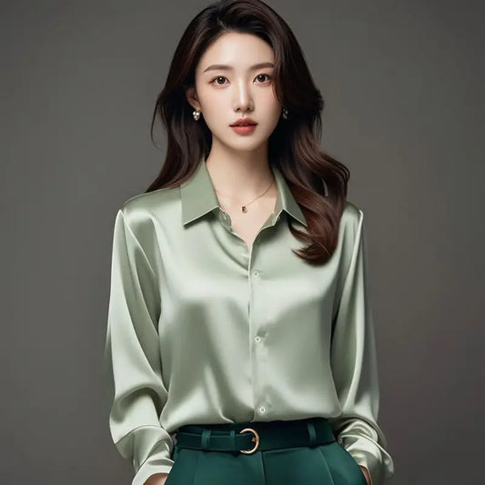 Woman wearing a light green satin shirt and green pants against a gray background