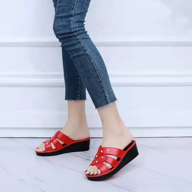 Red sandals worn with blue jeans on a light wooden floor.