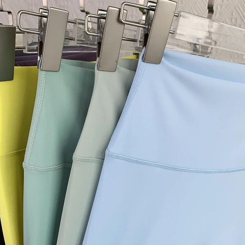 Four leggings in yellow, green, gray, and blue hanging on a rack.
