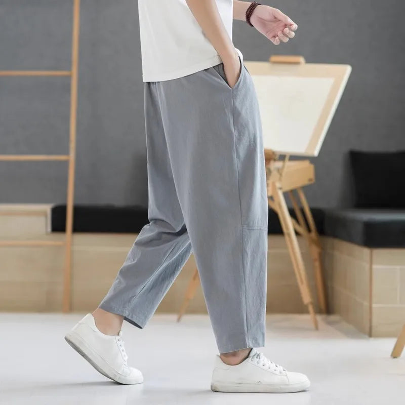 Person wearing gray pants and white sneakers in a room with wooden furniture and a gray wall.