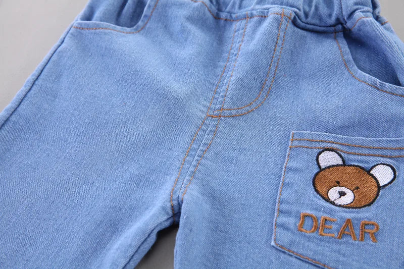 Blue denim shorts with a teddy bear design and 'DEAR' text on a neutral background