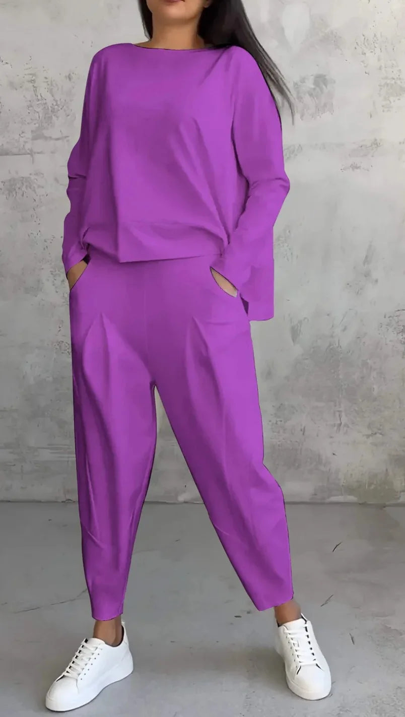 Person wearing a purple outfit with white sneakers against a gray concrete wall.