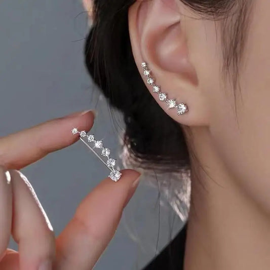 Close-up of a person wearing diamond stud earrings with one hand holding another pair.