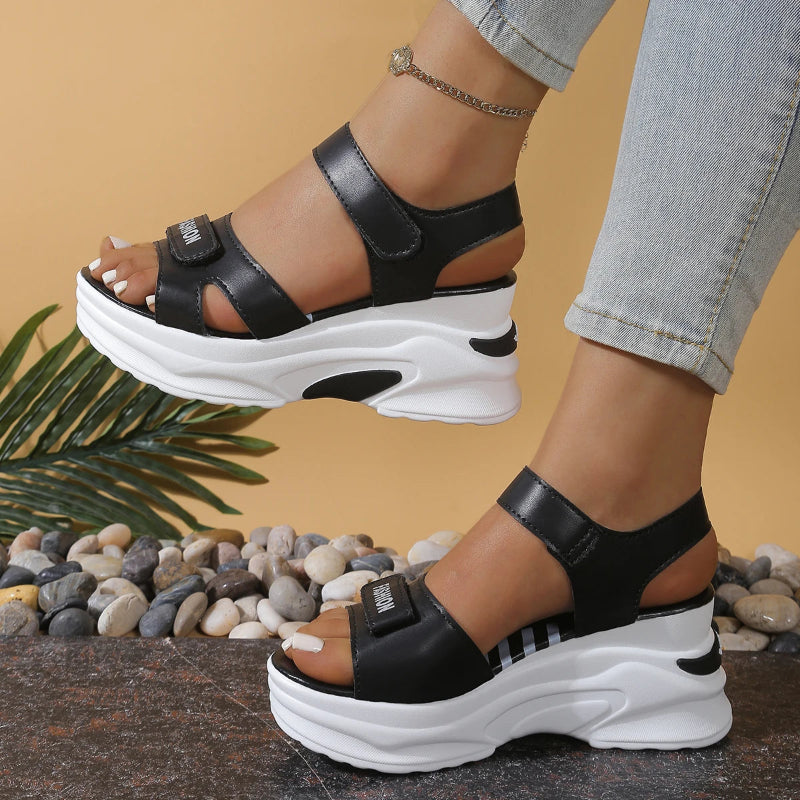 Black platform sandals with white soles worn by a person on a neutral background