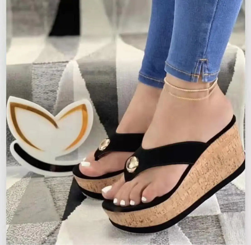 Black wedge sandals with cork sole worn by a person on a patterned floor.